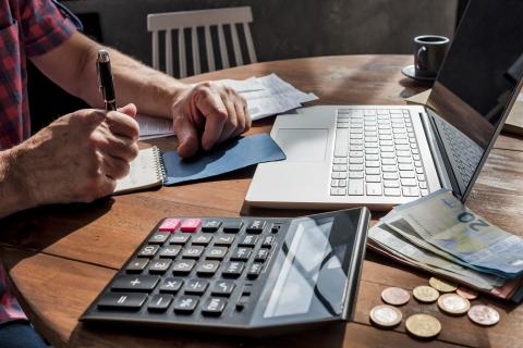 Man manually calculating for expenses with laptop and calculator 